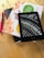 A Kindle device displaying a black and white image of a typewriter's keys is placed on top of a stack of two books with colorful covers. Next to the books is a pink pen, all resting on a wooden surface.