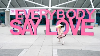 a girl is running in front of a sign that says everybody say love