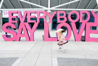 a girl is running in front of a sign that says everybody say love