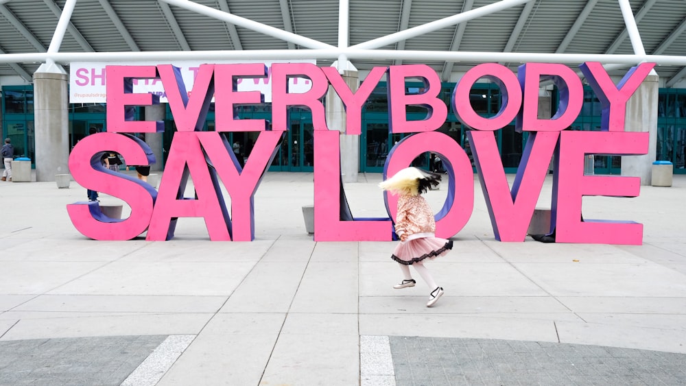 a girl is running in front of a sign that says everybody say love