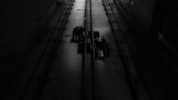 A dimly lit industrial setting with two cables running vertically along a textured floor. There are mechanical components in the center, casting shadows due to the minimal lighting.