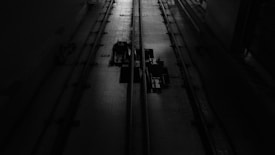 A dimly lit industrial setting with two cables running vertically along a textured floor. There are mechanical components in the center, casting shadows due to the minimal lighting.