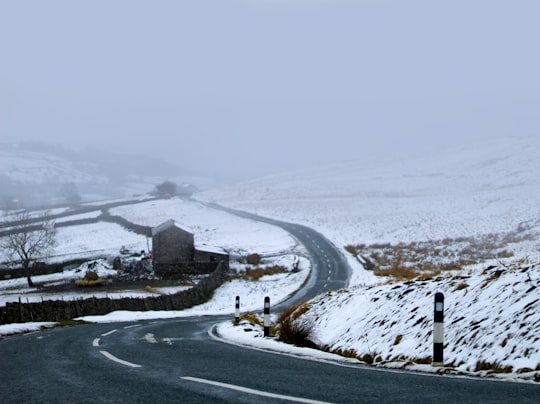 asphalt road between snow-covered field during daytime in Reeth United Kingdom