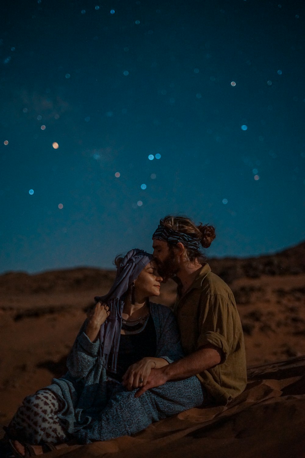 homme et femme assis sur le sable du désert sous le ciel bleu pendant la nuit