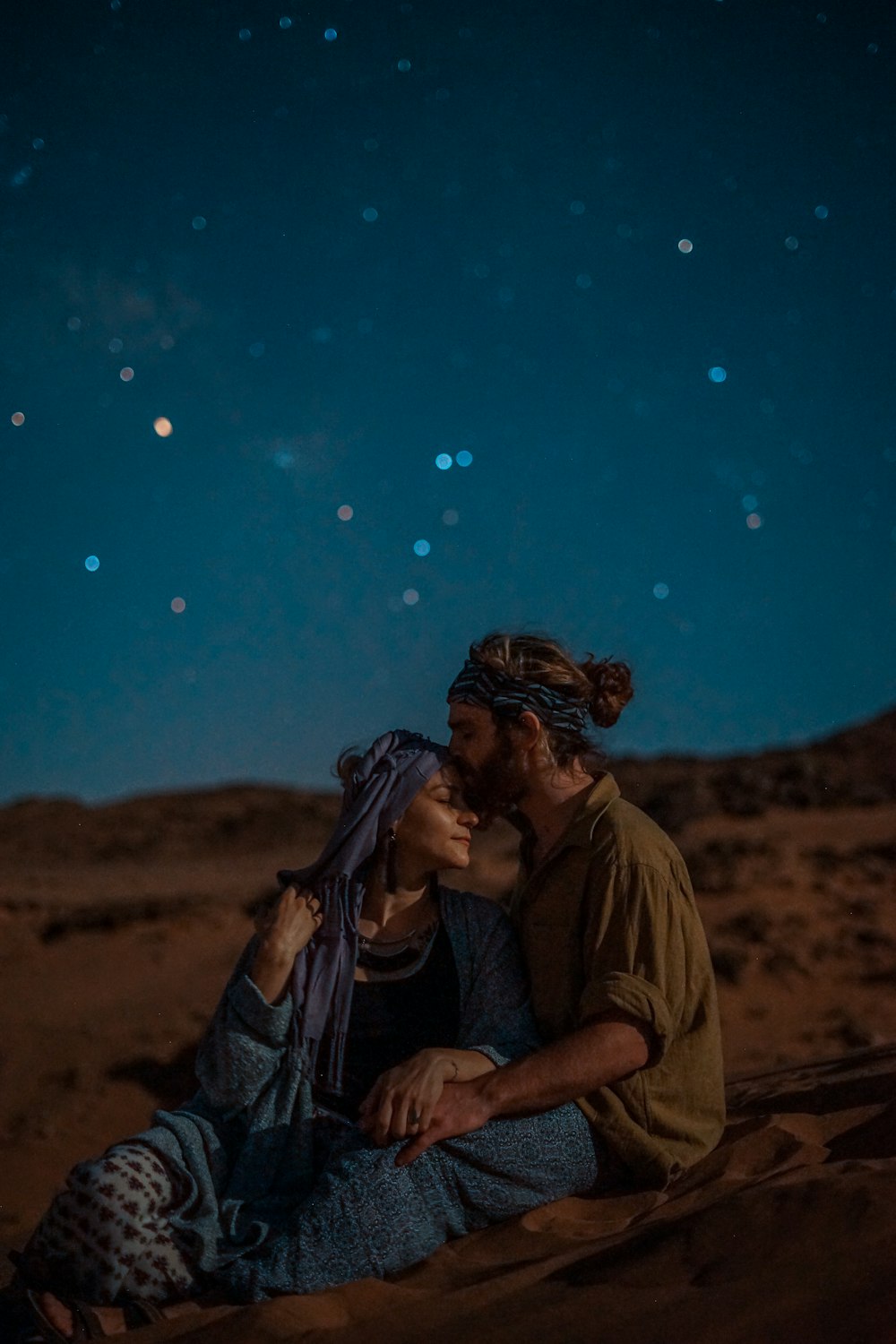 Mann und Frau sitzen nachts auf Wüstensand unter blauem Himmel