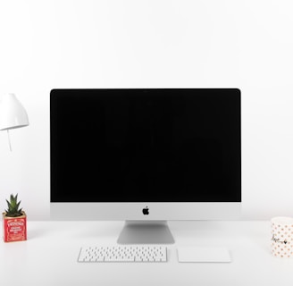 silver iMac, Apple Wireless Keyboard, and Apple Magic TrackPad near table lamp