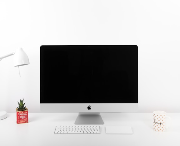 silver iMac, Apple Wireless Keyboard, and Apple Magic TrackPad near table lamp