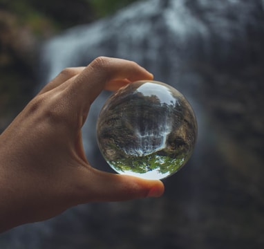 person holding glass globe beside water falls