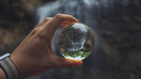 person holding glass globe beside water falls