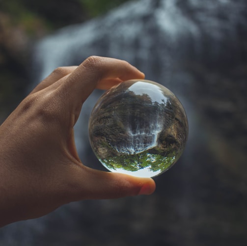 person holding glass globe beside water falls