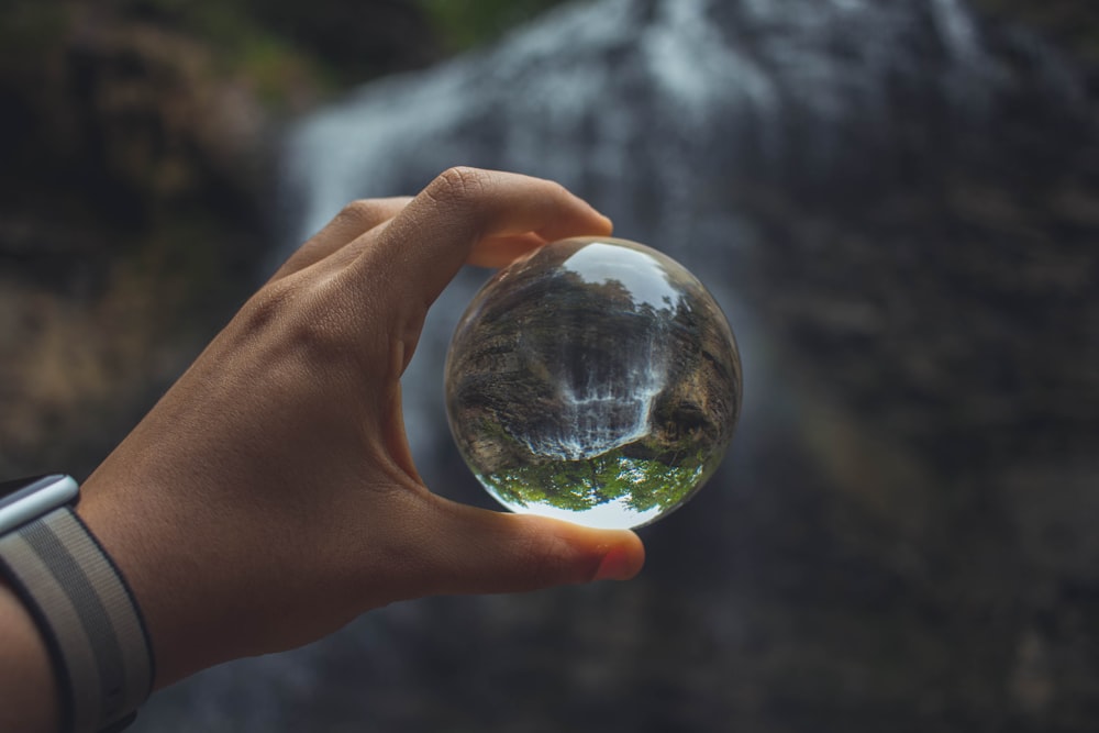 person holding glass globe beside water falls