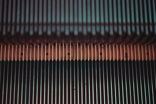 A close-up view of the mechanical components of an escalator, featuring a series of parallel metal steps and grooves with a combination of teal and brown hues.