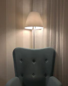 Elegant floor lamp with a slender design standing beside a comfy armchair.