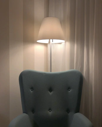Elegant floor lamp with a slender design standing beside a comfy armchair.