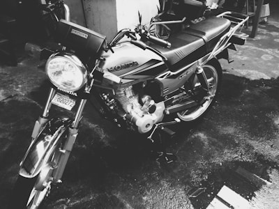 A motorcycle with a Honda logo is parked on a wet surface. The image is in black and white, highlighting the bike's design and chrome detailing. The vehicle appears clean and polished, reflecting the surroundings on its metallic parts.