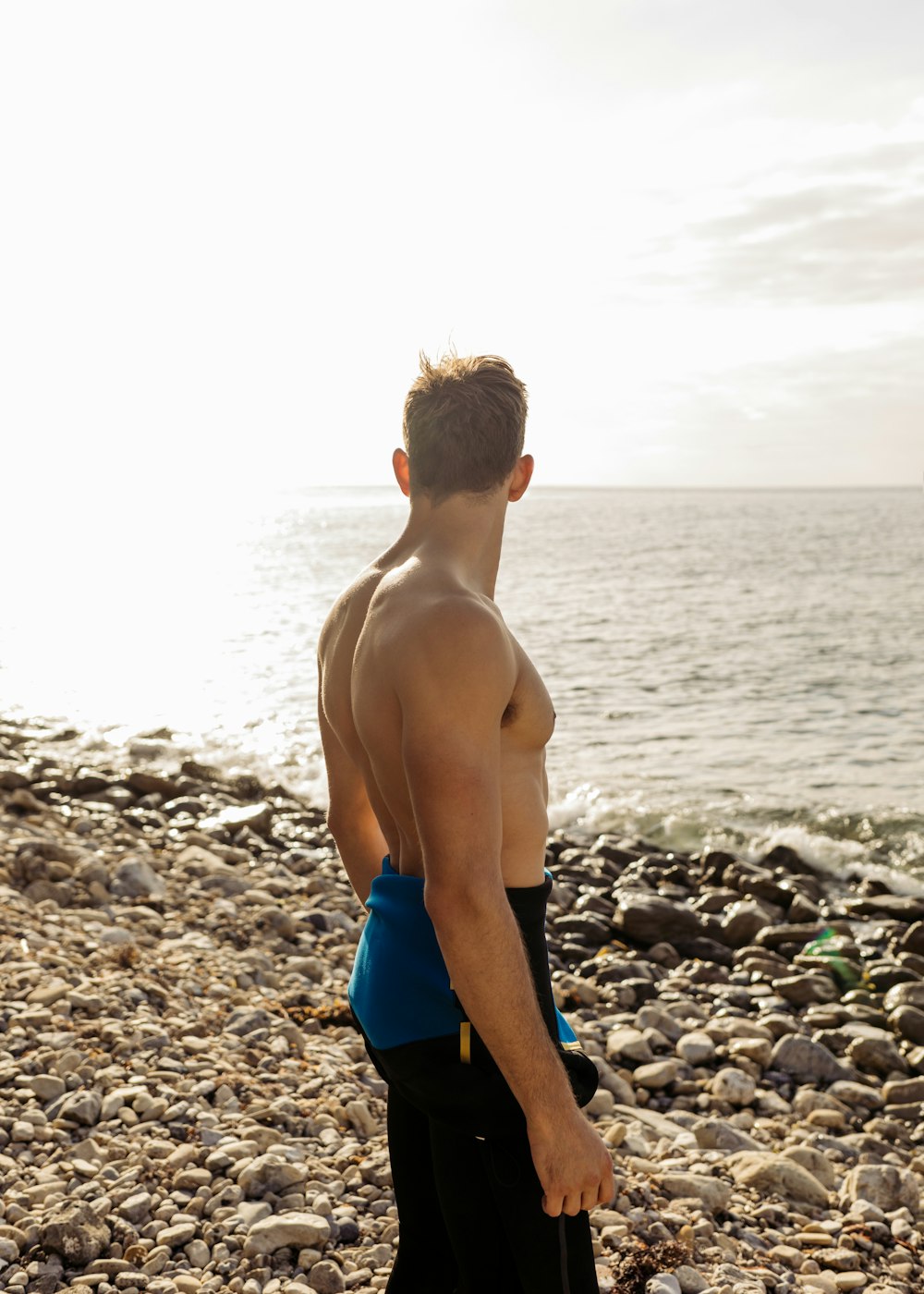 man in blue and black bottoms standing on beach