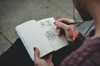 Close-up of a hand sketching story ideas in a notebook with gentle watercolor illustrations around.