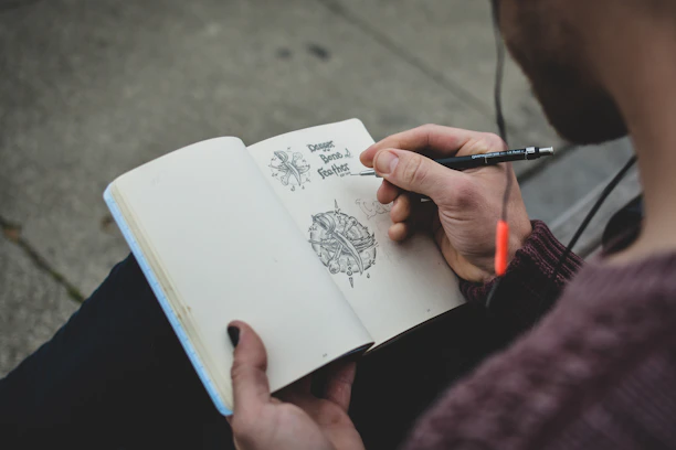 Artist's hand drawing a detailed sketch inside a Kertaskosong sketchbook.