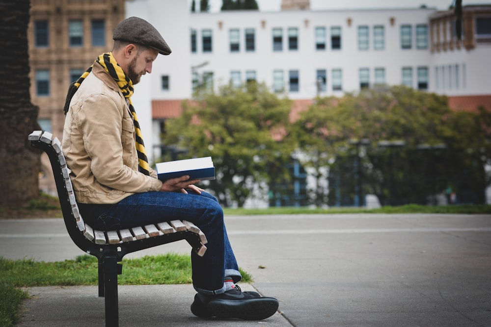 homme lisant un livre assis sur un banc à l’extérieur