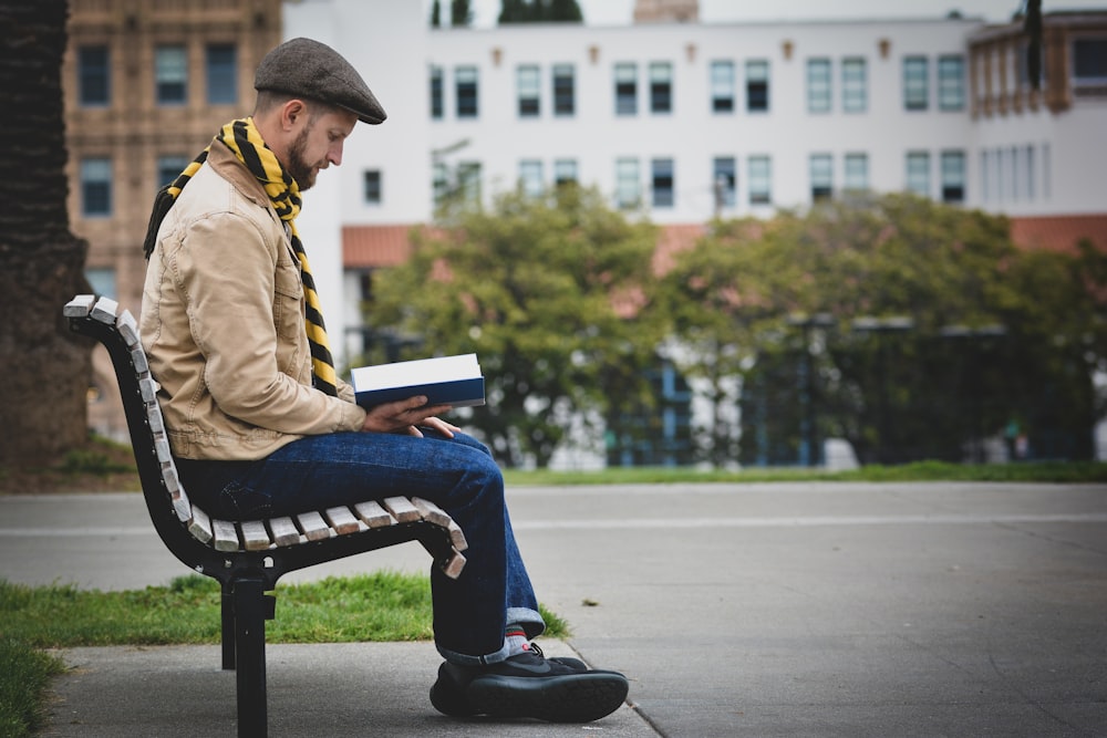 uomo che legge il libro mentre è seduto sulla panchina all'aperto