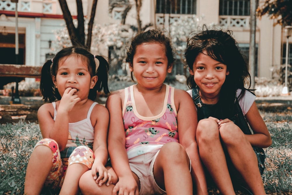 three young girls sitting on the ground in front of a building