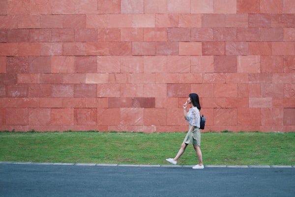 Jeune femme marche à pied et mange une glace devant un grand mur rouge