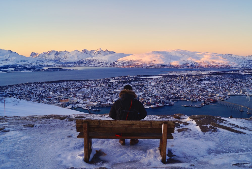 茶色の木製のベンチに座って景色を眺めている人