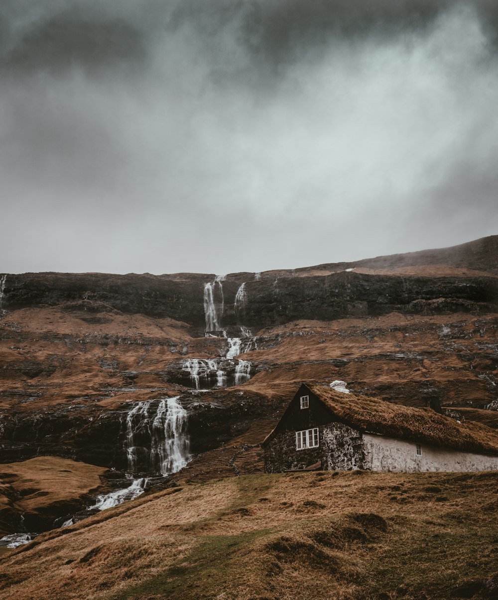 waterfalls near wooden house under gray skies