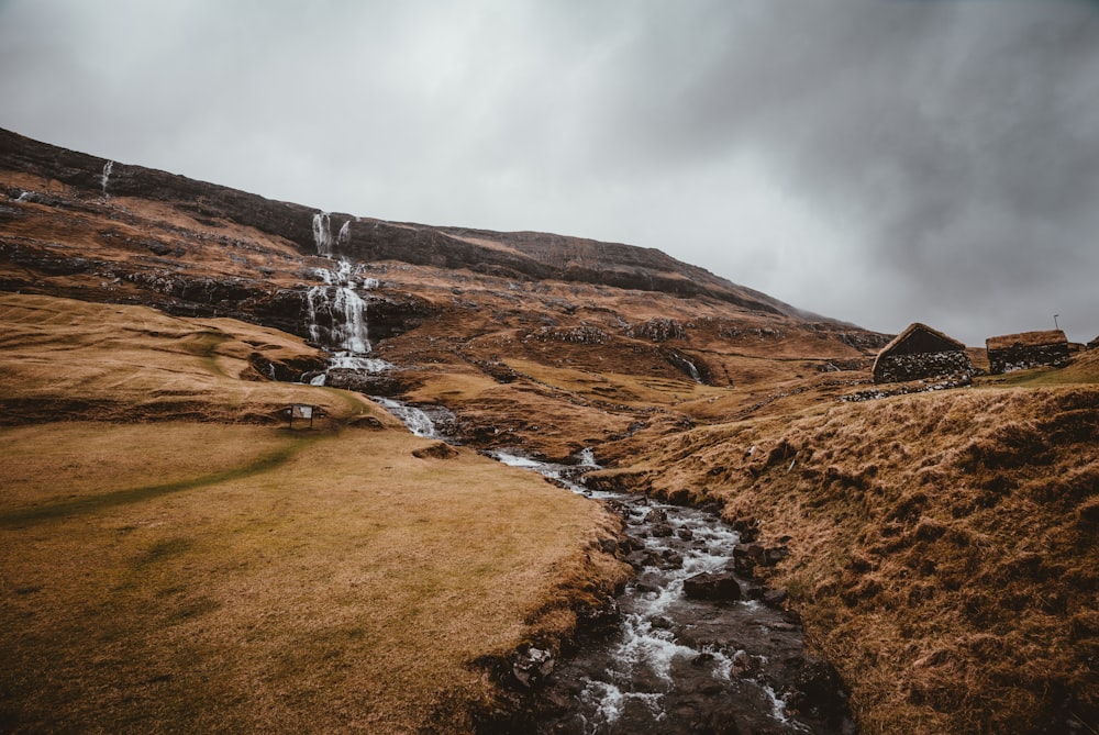 river near two brown houses under cloudy sky