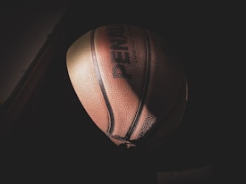 A basketball is positioned against a dark background, partially illuminated by a soft light that highlights its textured surface and seams.