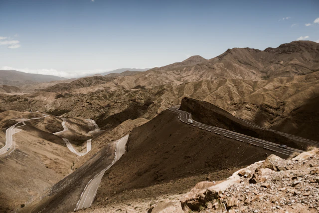 Route de montagne longeant la rivière de la vallée de l'Ourika avec des villages berbères en terre sur les pentes