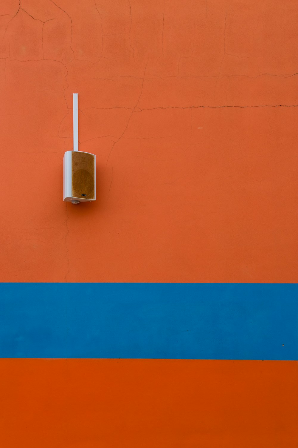オレンジ色に塗られた壁に取り付けられた白いスピーカー