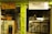 A small, cozy café features a wooden counter and shelves filled with organic products. The café's signage emphasizes natural and intelligent cooking. A person wearing a headscarf stands behind the counter, with stools lined up for customers.