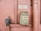 An old emergency phone mounted on a textured pink wall. It features a worn-out rectangular housing with an instruction label in French. Nearby, a metal pipe runs vertically alongside the wall.