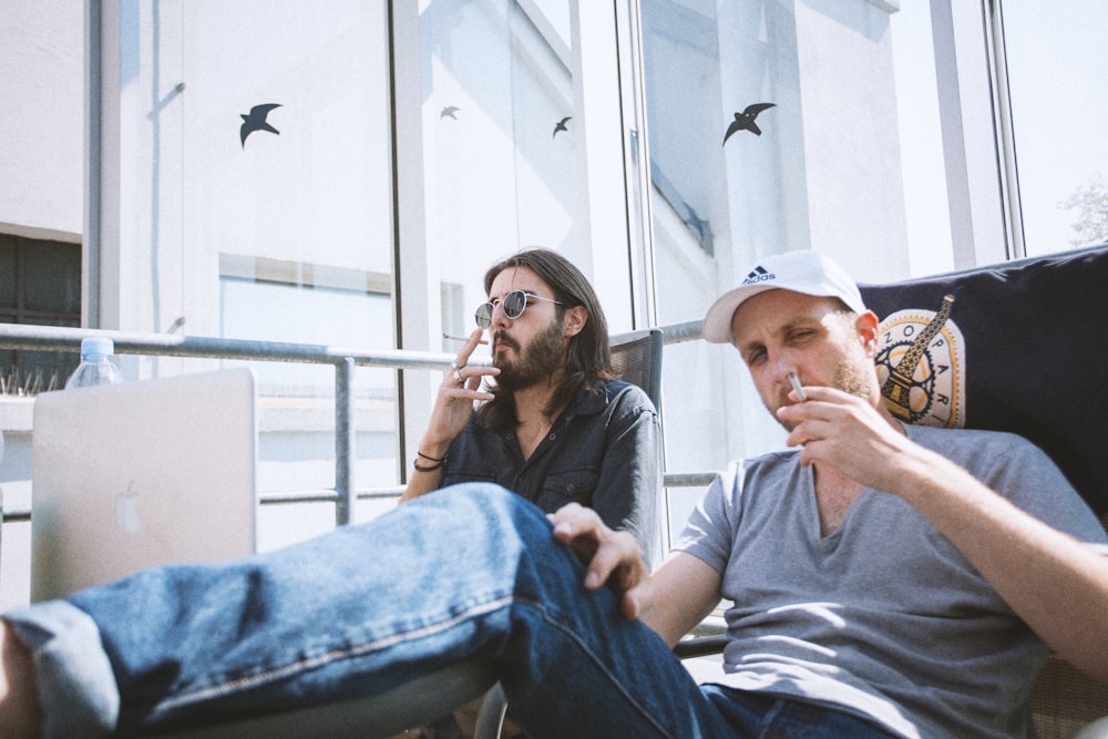 two mens doing smoke while sitting inside building at daytime