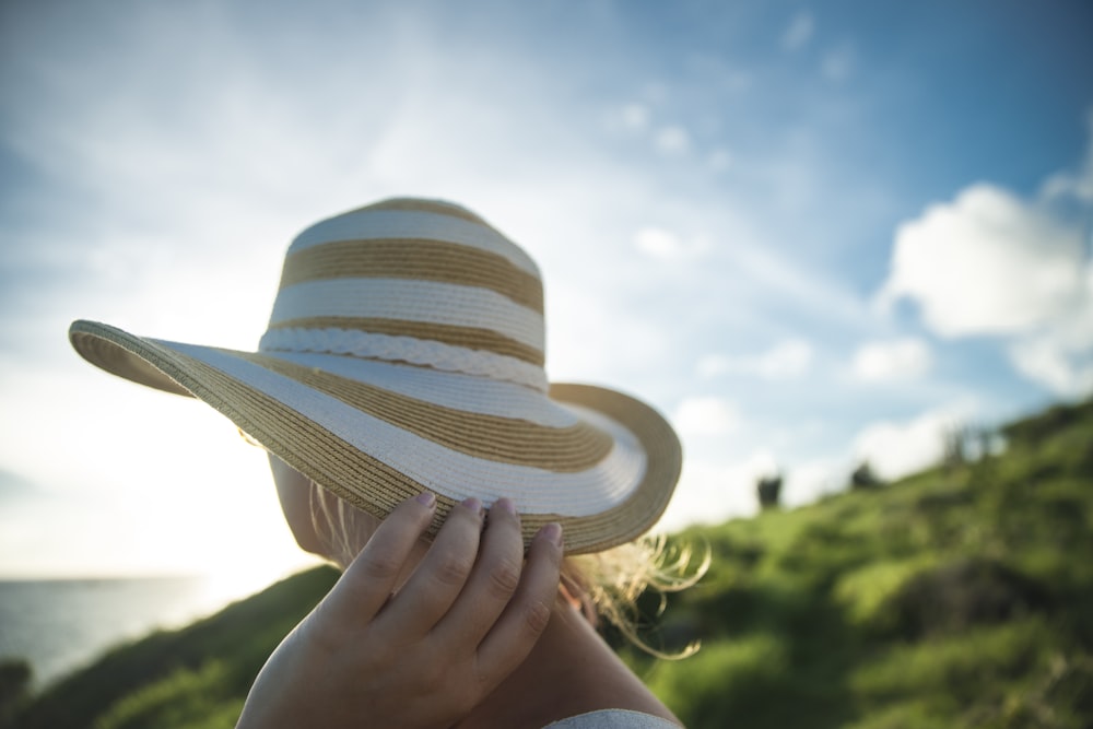 woman holding beige and gray sun hat