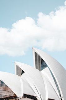 A close-up view of the Sydney Opera House's iconic, white-shelled roofs set against a clear blue sky with scattered clouds.