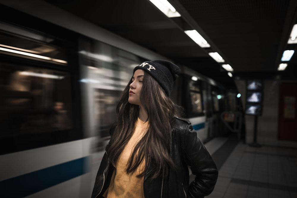 woman putting her hand on jacket pocket while standing beside train at station