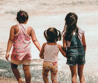 three girls holding each other hand walking towards brown soil