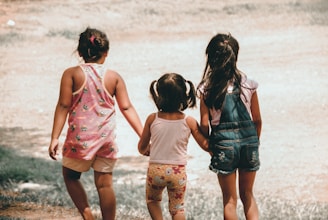 three girls holding each other hand walking towards brown soil