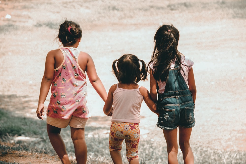 três meninas segurando uma à outra de mãos caminhando em direção ao solo marrom