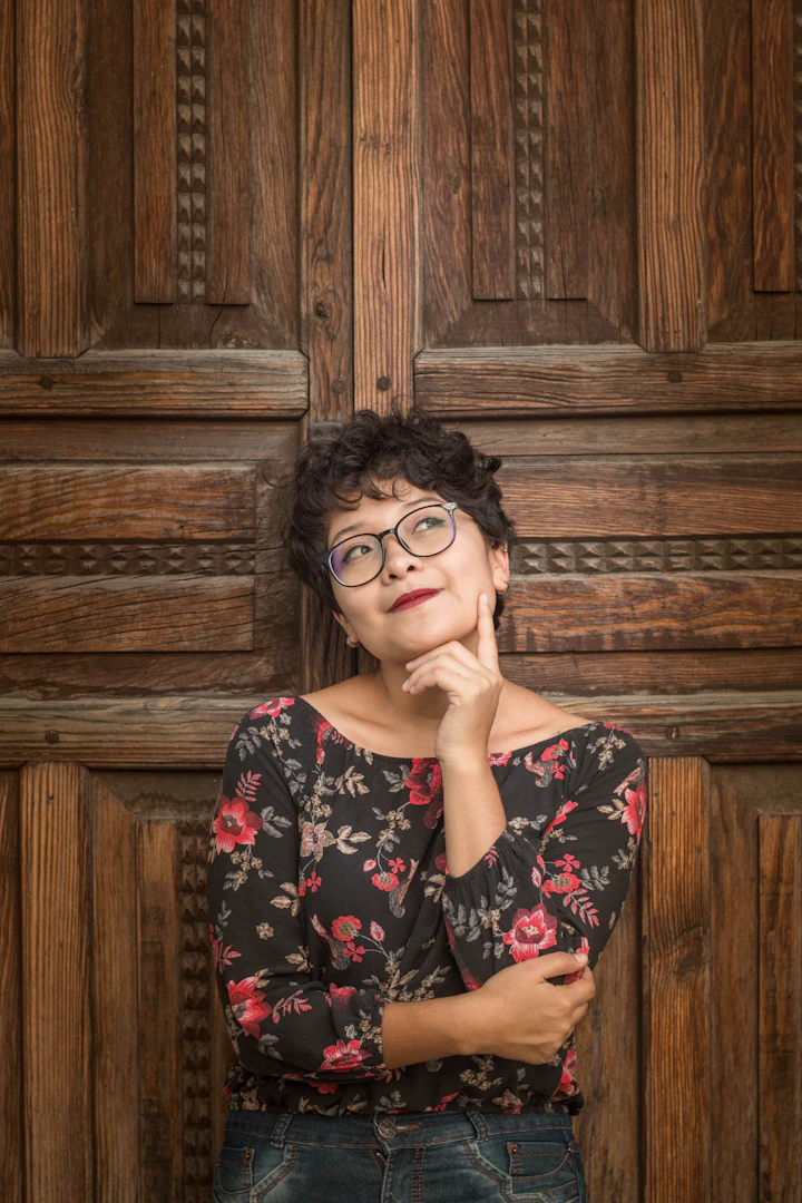 Woman leaning against a door, hand on her cheek, thinking