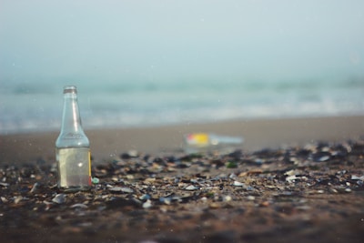 A clear bottle filled with seawater placed on a sandy beach.