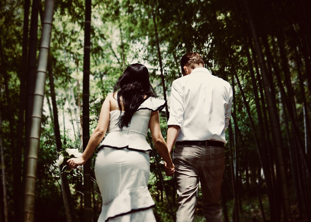 man and woman holding hands while walking near trees