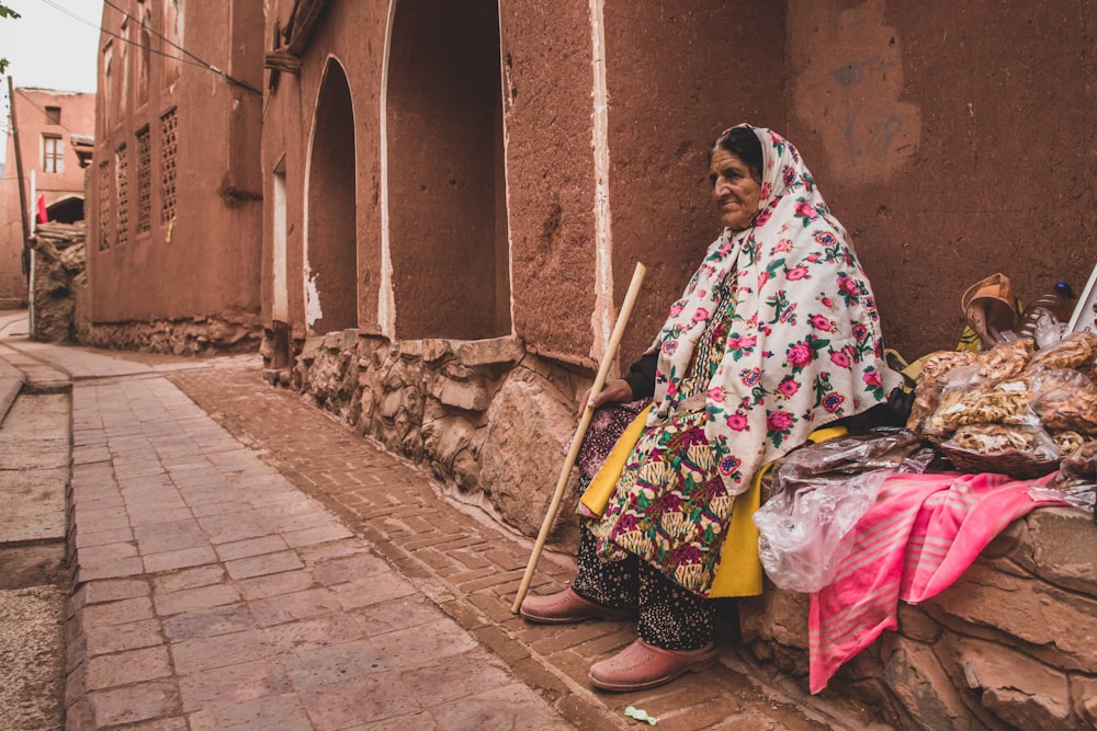 Mujer con tocado de hiyab floral blanco y rosa sentada en cemento
