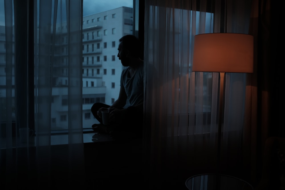 man sitting beside glass window near high rise building
