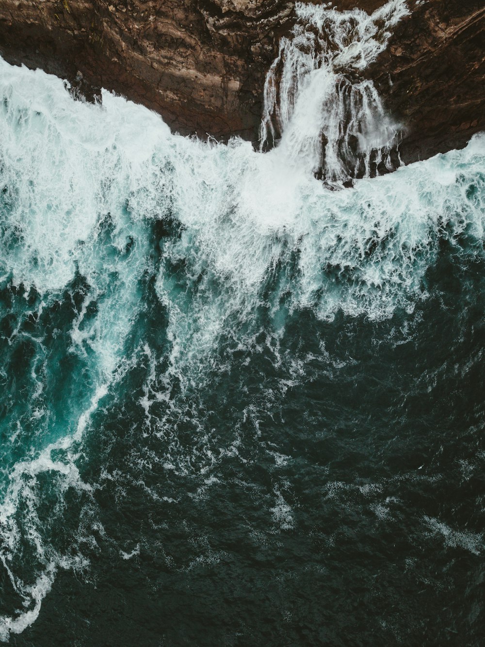 body of water crashing on brown rock mountain during daytime