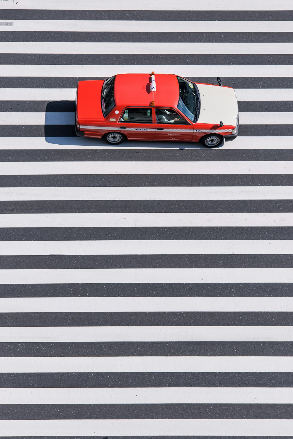 Une berline rouge et blanche passe sur une voie piétonne