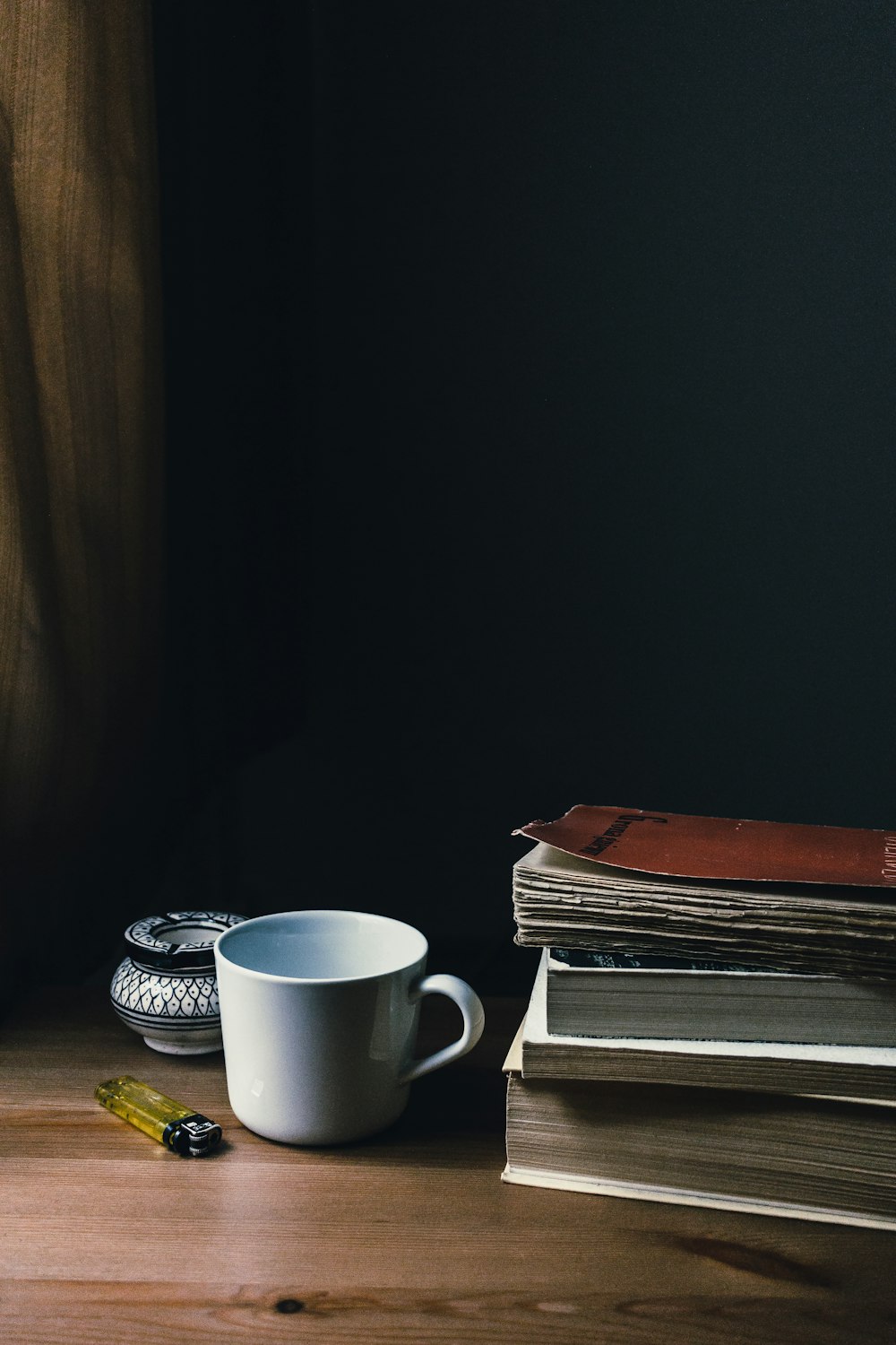 Taza de cerámica blanca junto a libros y encendedor desechable