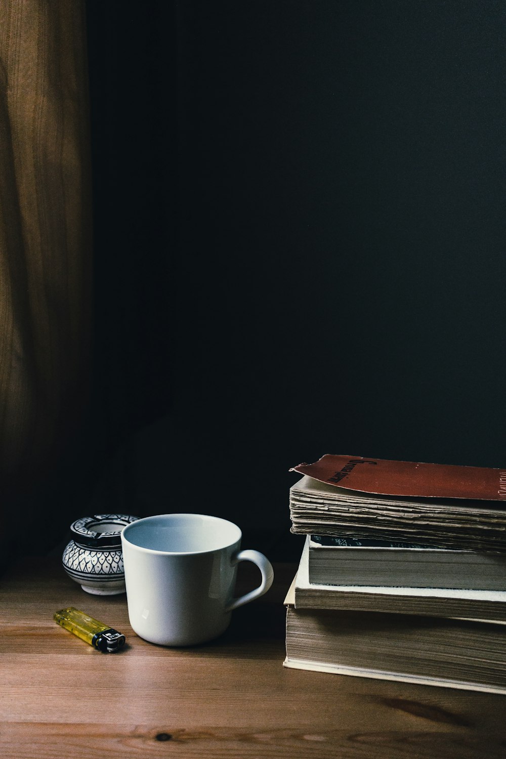 white ceramic mug beside books and disposable lighter
